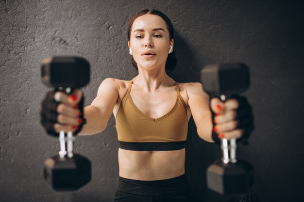 Young attractive woman exercising with dumbbells at the gym