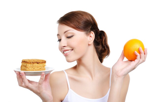 식욕을 돋 우는 케이크와 건강 한 오렌지를 들고 젊은 매력적인 여자