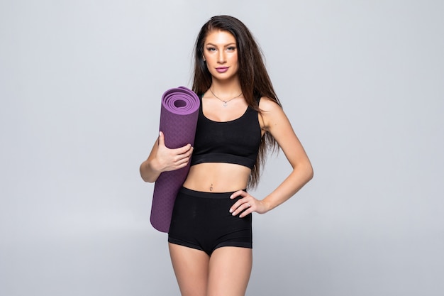 Молодая привлекательная женщина держа циновку йоги изолированный