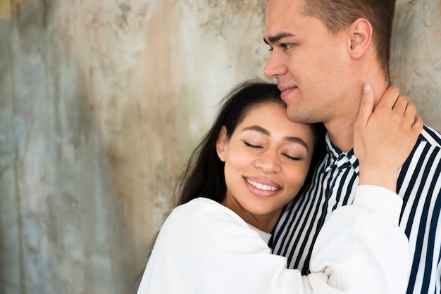 Free photo young attractive woman hugging boyfriend against concrete wall