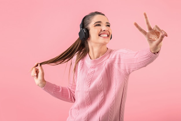 ピンクのセーターを着てワイヤレスヘッドフォンで音楽を聴いている若い魅力的な女性笑顔