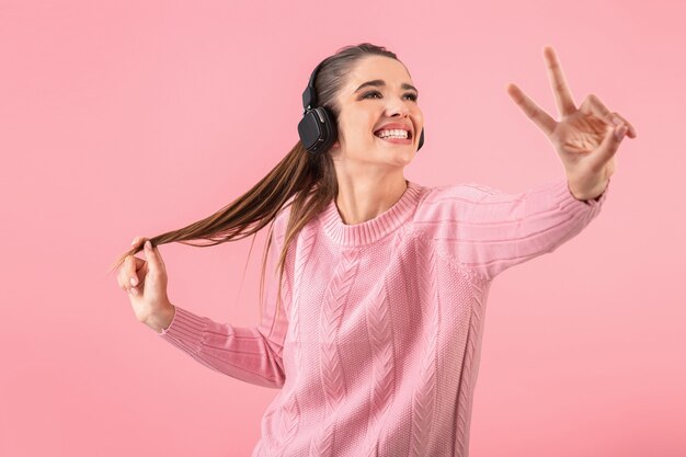 Молодая привлекательная женщина слушает музыку в беспроводных наушниках в розовом свитере улыбается