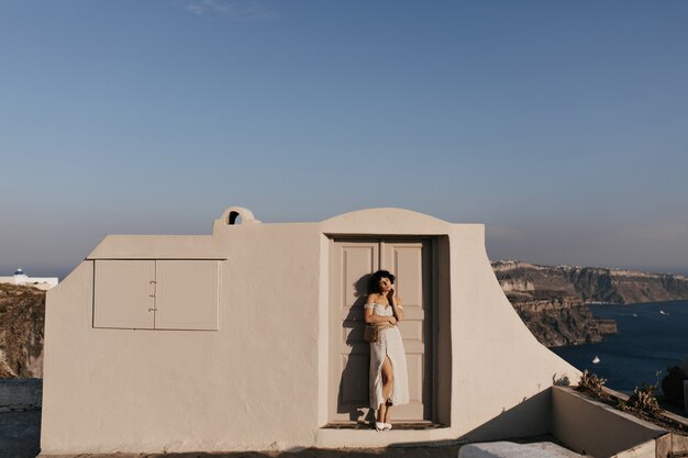 Young attractive woman in midi dress poses near beige house