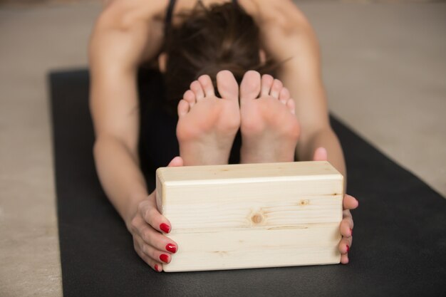 Young attractive woman in paschimottanasana pose with block, gre