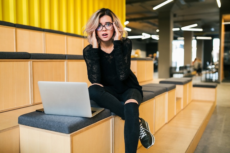 Free Photo young attractive woman sitting in lecture hall, having stress, working on laptop, wearing glasses, modern auditorium, student education online, freelancer, busy, headache, frustrated face expression