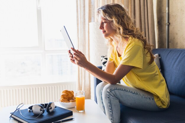 Young attractive woman sitting relaxed on sofa at home holding tablet, watching online