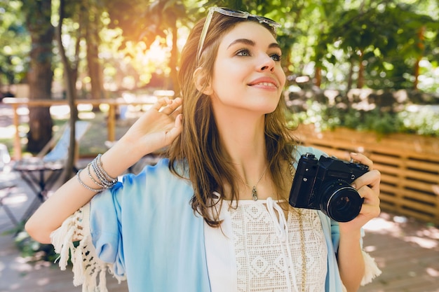 Молодая привлекательная женщина в летнем модном наряде фотографирует с ретро камерой