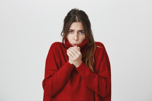Молодая привлекательная женщина в свитере чувствует себя холодно, дует воздух на руки для разогрева
