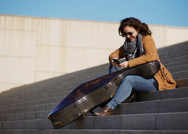 Young attractive woman using her smartphone with musical instrument