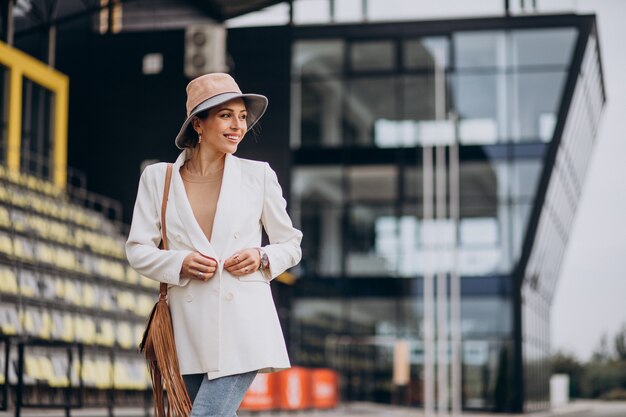 屋外を歩く白いジャケットの若い魅力的な女性