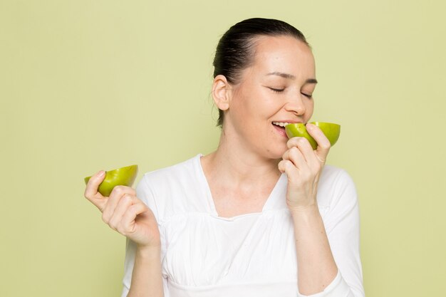 Молодая привлекательная женщина в белой рубашке держит и ест нарезанные зеленые яблоки