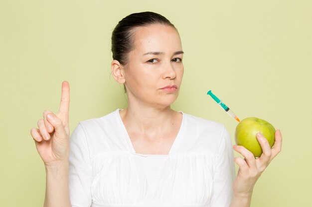 Young attractive woman in white shirt holding green apple with syringe