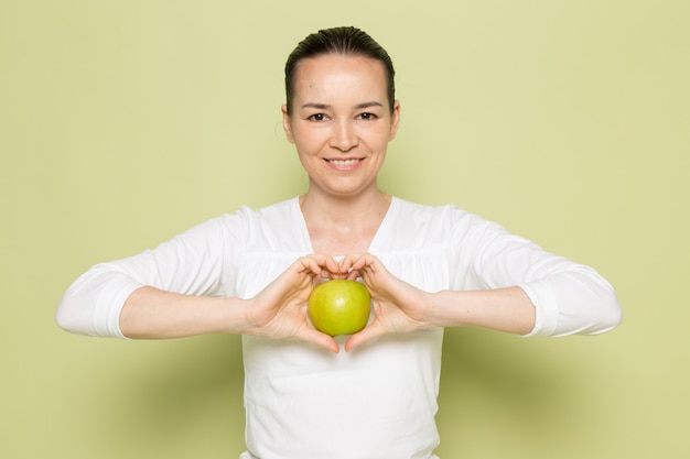 Молодая привлекательная женщина в белой рубашке держит зеленое яблоко