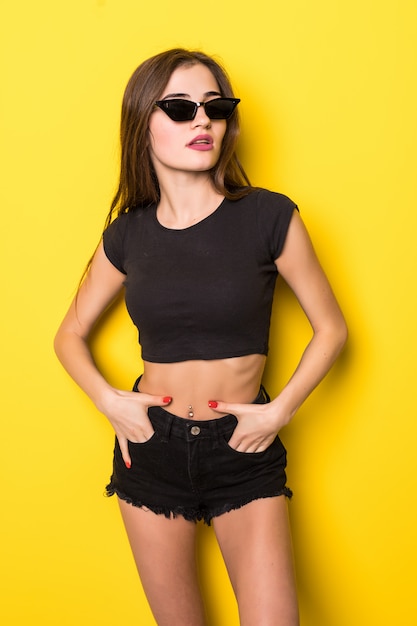 Young attractive woman in white top with lollipop in hand on yellow wall