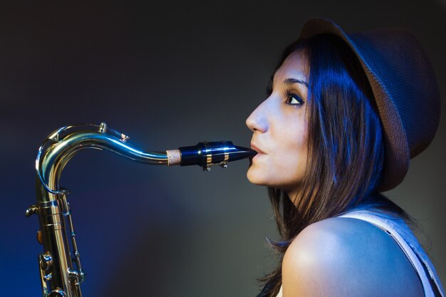 Молодая привлекательная женщина в шляпе играет на саксофоне