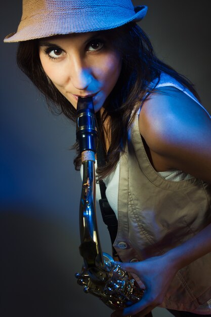 Young and attractive woman with hat playing the saxophone