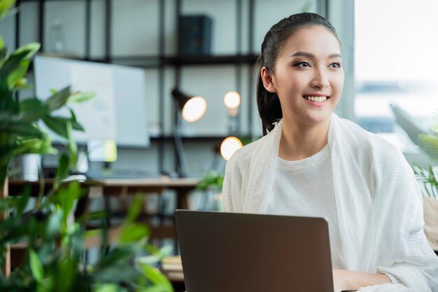 집에서 일하는 젊은 매력적인 아시아 여성은 태블릿을 사용하여 비즈니스 데이터 차트 계획 보고서를 확인하고 여가와 함께 거실 홈 격리 개념에서 소파에서 휴식을 취합니다.