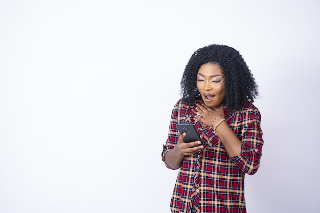 Young back woman holding her phone looking shocked and worried.