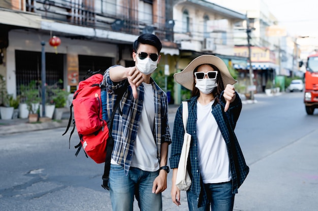 Young backpacker couple in face mask and sunglasses make a prohibition cross mark with thump down