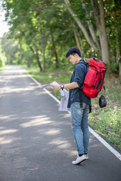 地図を持つ若いバックパッカーの男の旅行者、彼は森林試験、コピースペースで夏休みに屋外でリラックスしながら大きなバックパックを運ぶ