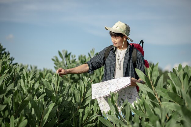 地図を持つ若いバックパッカーの男の旅行者、彼は森林試験、コピースペースで夏休みに屋外でリラックスしながら大きなバックパックを運ぶ