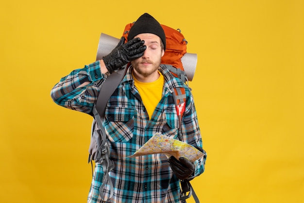 young backpacker with black hat holding map covering eye with hand