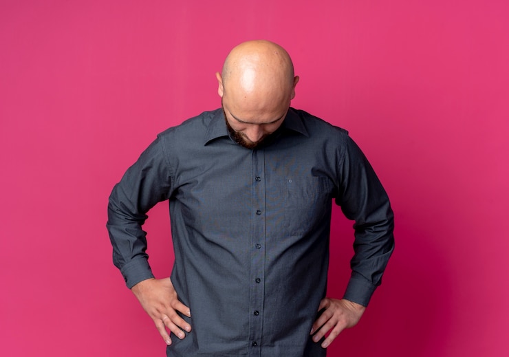 Free Photo young bald call center man putting hands on waist looking down isolated on crimson background with copy space