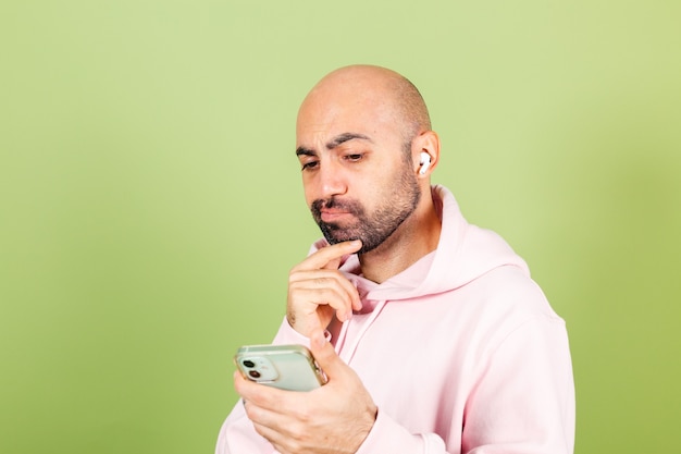 Young bald caucasian man in pink hoodie isolated, hold phone thoughtful hold chin