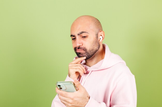 Young bald caucasian man in pink hoodie isolated, hold phone thoughtful hold chin