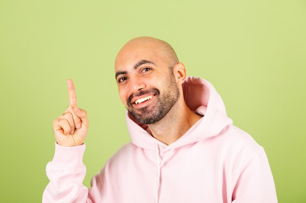 Young bald caucasian man in pink hoodie isolated, look with smile point fingers up