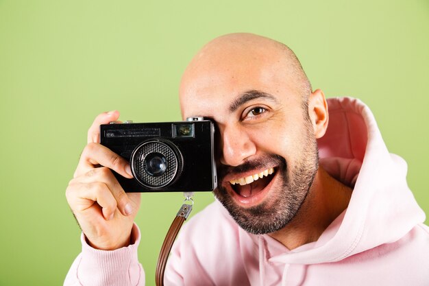 Молодой лысый кавказский мужчина в розовой толстовке с капюшоном изолировал, позитивный хипстер держит камеру