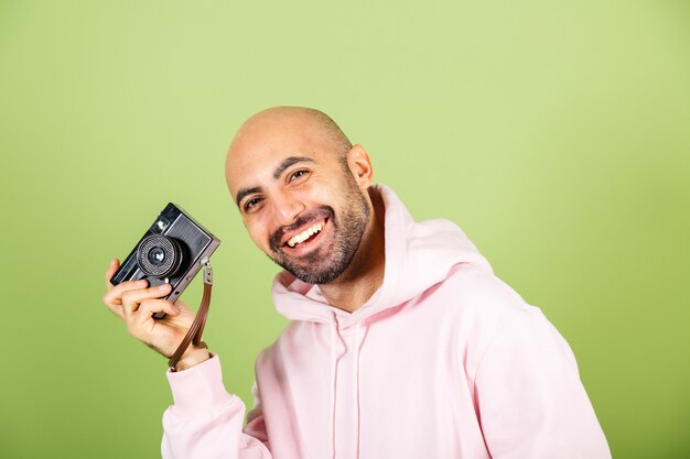 Young bald caucasian man in pink hoodie isolated, positive hipster hold camera