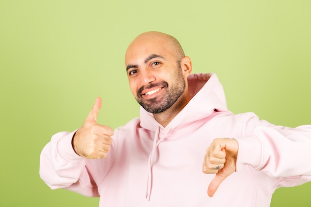 Young bald caucasian man in pink hoodie isolated, positive one thumb  up one down