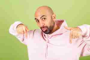 Free photo young bald caucasian man in pink hoodie isolated, positive shocked amazed  excited point fingers down