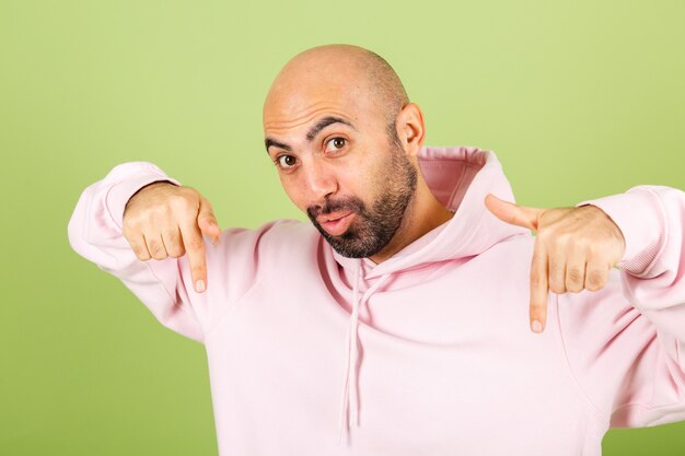Young bald caucasian man in pink hoodie isolated, positive shocked amazed  excited point fingers down