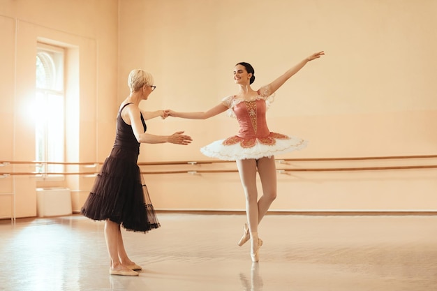 Young ballerina holding hand with her instructor while practicing in ballet studio