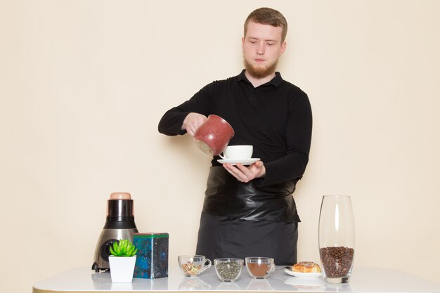 young barista in black working suit with ingredients and coffee equipment brown coffee seeds on white