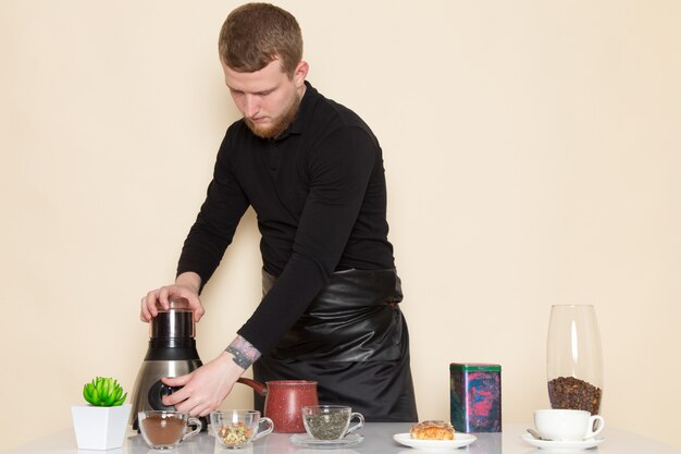 young barista in black working suit with ingredients and coffee equipment brown coffee seeds on white