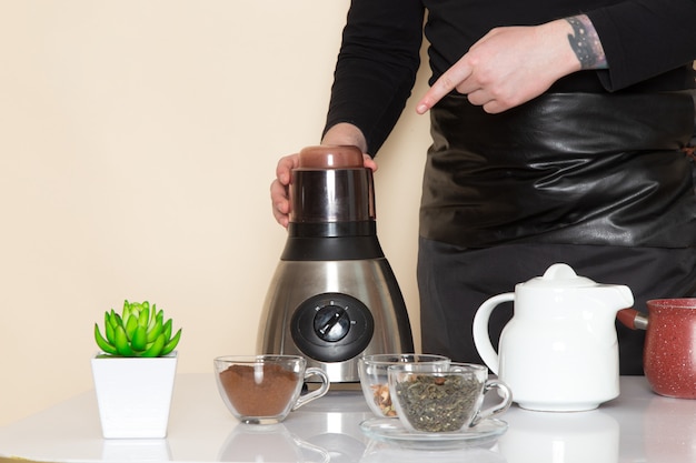 Young barista in black working suit with ingredients and coffee equipment brown coffee seeds on white