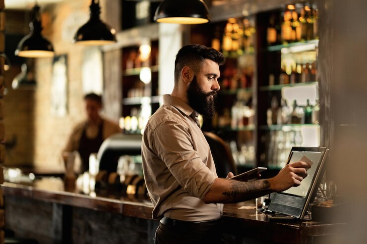 Free Photo young bartender using cash register at bar counter in a pub.