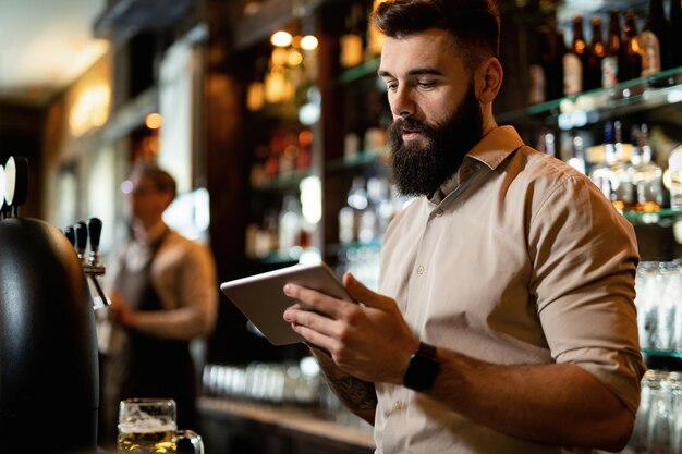 술집에서 일하는 동안 디지털 태블릿을 사용하는 젊은 바텐더