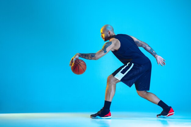 Молодой баскетболист команды в спортивной тренировке, практикующий в действии, изолированный на синей стене в неоновом свете