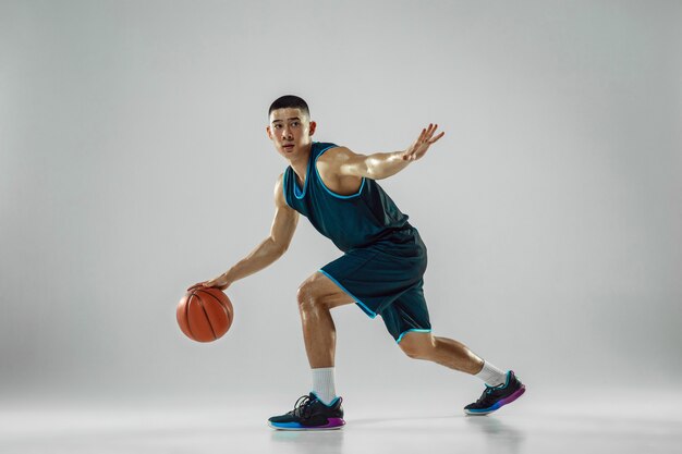 Young basketball player of team wearing sportwear training, practicing in action, motion in run isolated on white wall. Concept of sport, movement, energy and dynamic, healthy lifestyle.