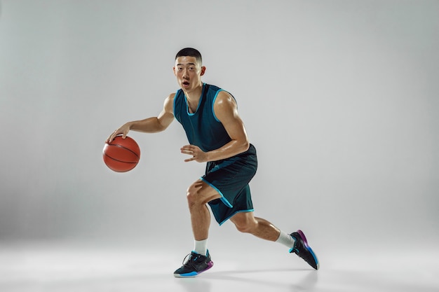 Free photo young basketball player of team wearing sportwear training, practicing in action, motion in run isolated on white wall. concept of sport, movement, energy and dynamic, healthy lifestyle.