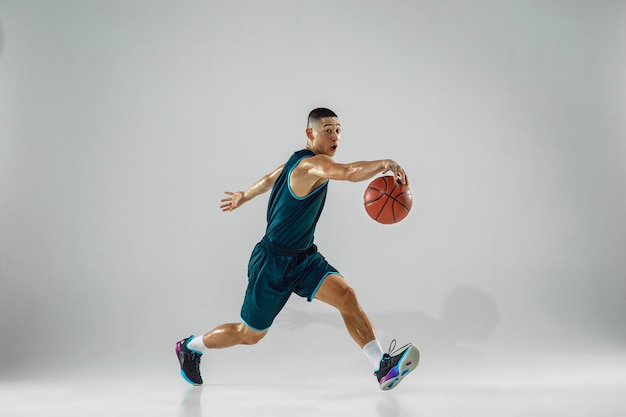 Young basketball player of team wearing sportwear training, practicing in action, motion in run isolated on white wall. Concept of sport, movement, energy and dynamic, healthy lifestyle.