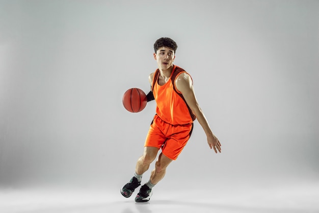 Free photo young basketball player of team wearing sportwear training, practicing in action, motion in run isolated on white wall. concept of sport, movement, energy and dynamic, healthy lifestyle.