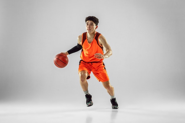 Young basketball player of team wearing sportwear training, practicing in action, motion in run isolated on white wall. Concept of sport, movement, energy and dynamic, healthy lifestyle.