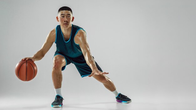 Young basketball player of team wearing sportwear training, practicing in action, motion in run isolated on white wall