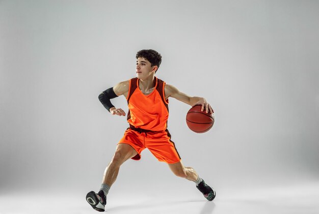 Young basketball player of team wearing sportwear training, practicing in action, motion in run isolated on white wall