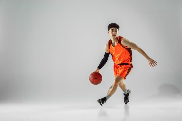 Young basketball player of team wearing sportwear training, practicing in action, motion in run isolated on white wall